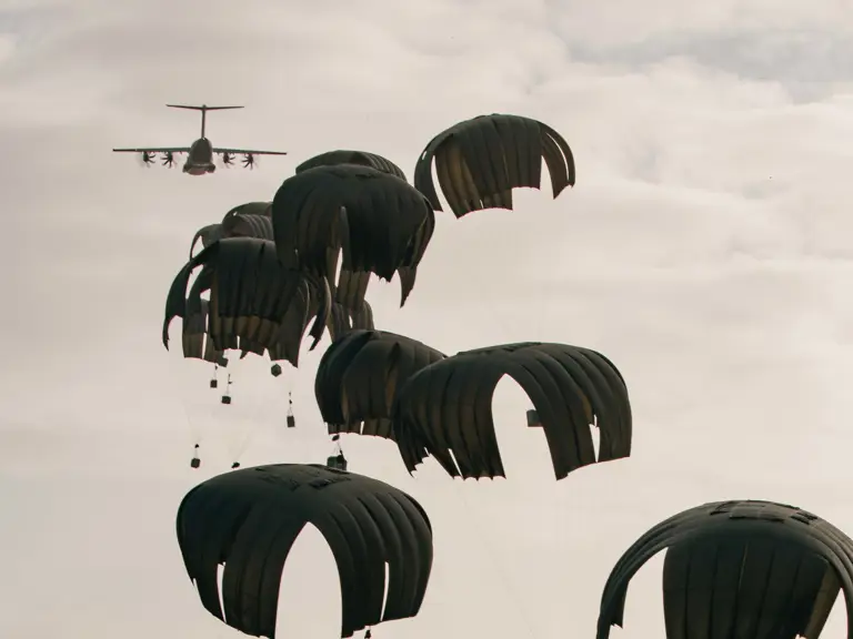 A group of parachutes descends towards the ground, each carrying a piece of cargo.
