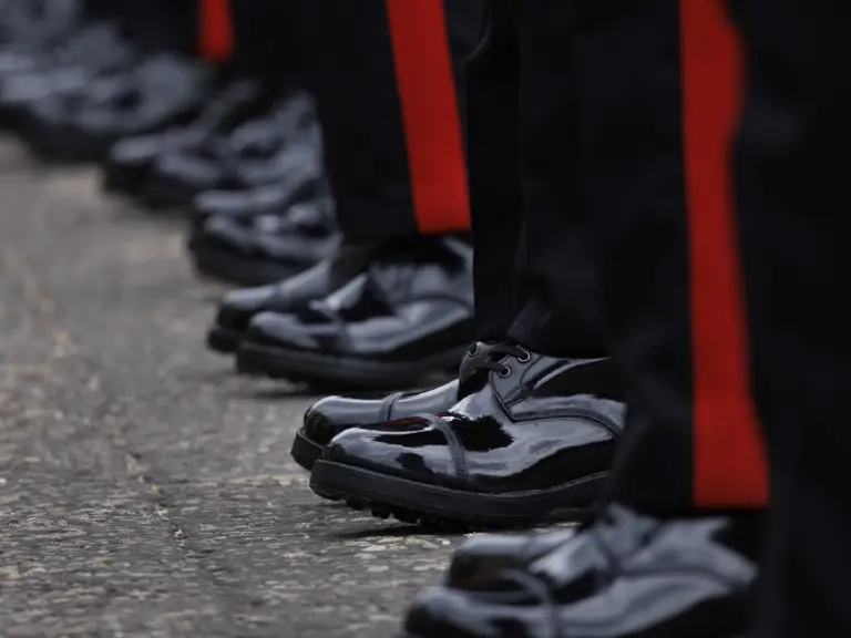 A row of black, polished dress shoes with red-striped trousers, worn by individuals.
