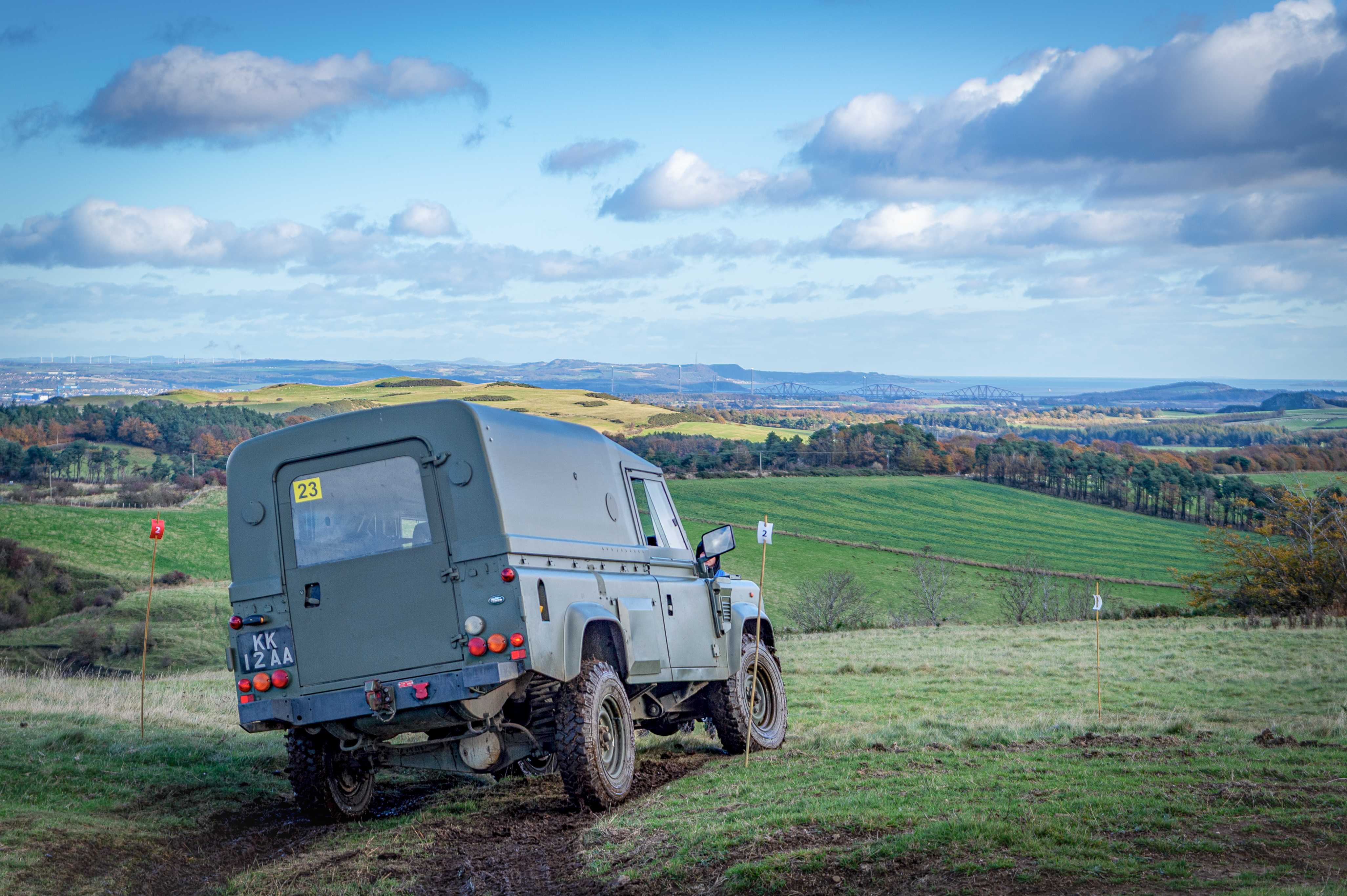 Off-road vehicle on a grassy hilltop, surrounded by rolling green fields under a blue sky with scattered clouds, evoking a sense of adventure.