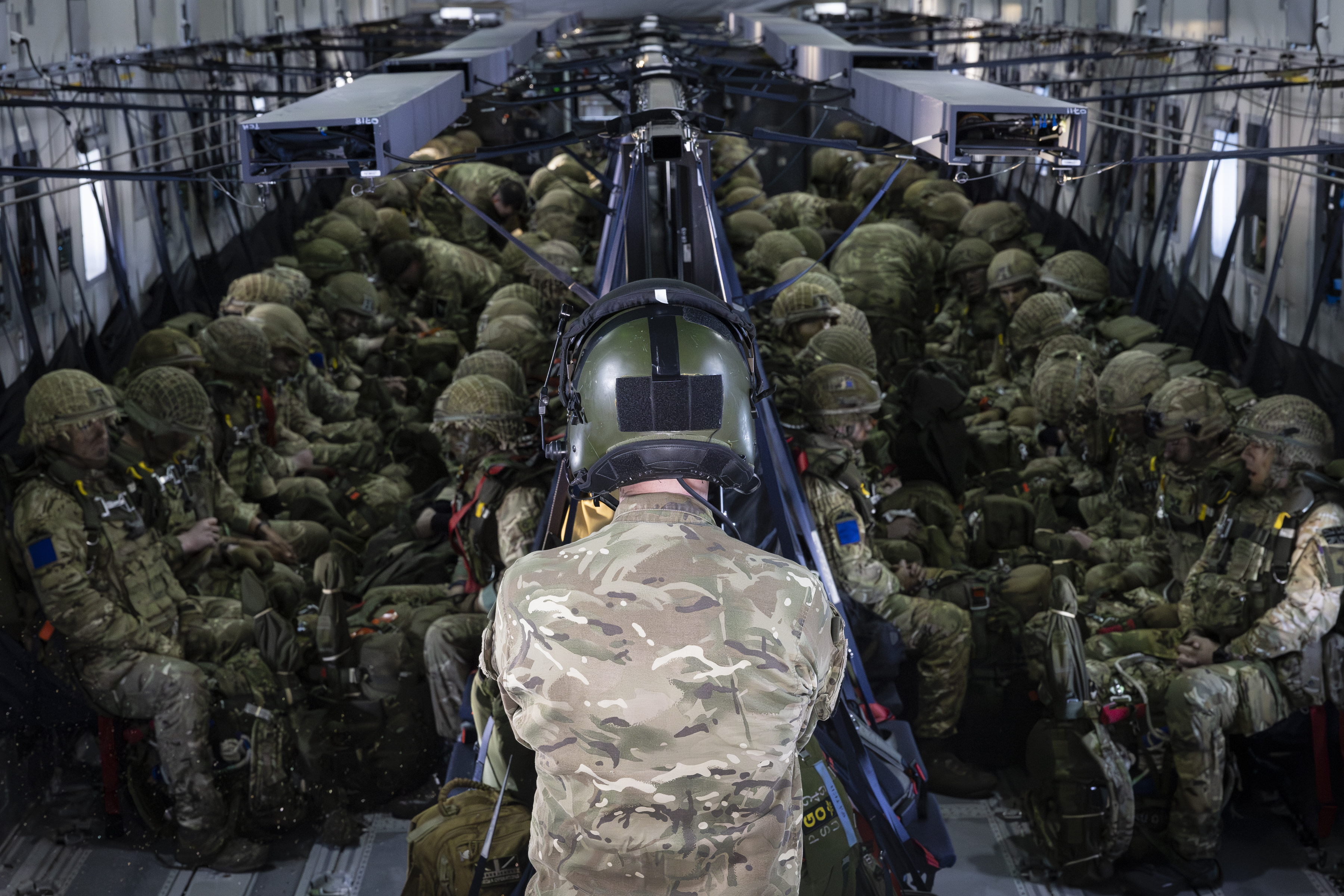 Soldiers in full combat gear seated inside a military transport aircraft preparing for deployment.