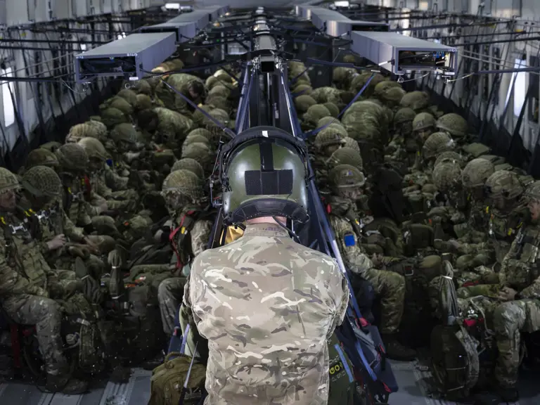 Soldiers in full combat gear seated inside a military transport aircraft preparing for deployment.