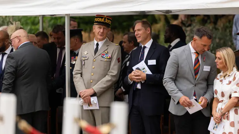 A group of people are gathered under a canopy, engaged in conversation. One person is wearing a military uniform.