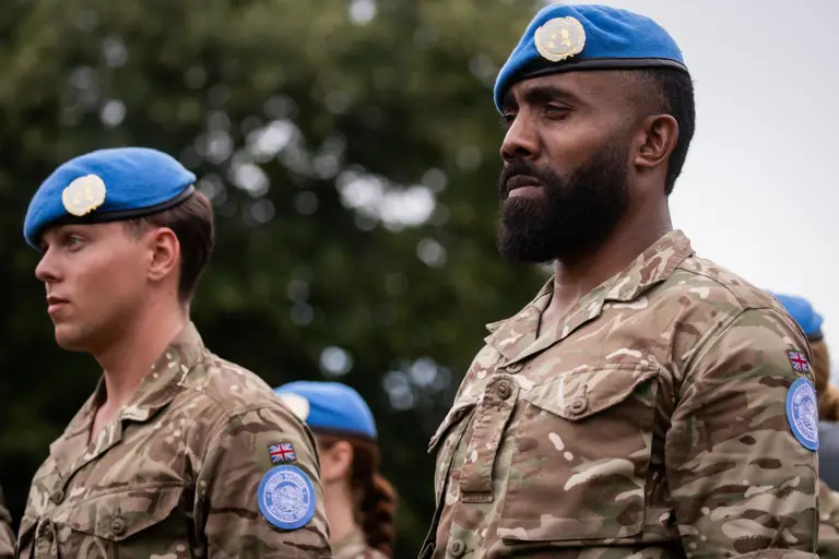 Two soldiers in camouflage uniform wear a blue beret on their heads.