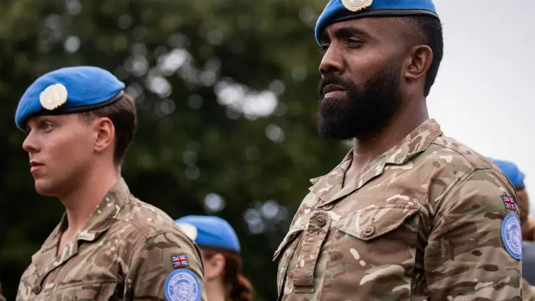 Two soldiers in camouflage uniform wear a blue beret on their heads.