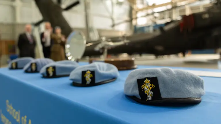 A row of light blue berets sit on a table with a blue tablecloth.