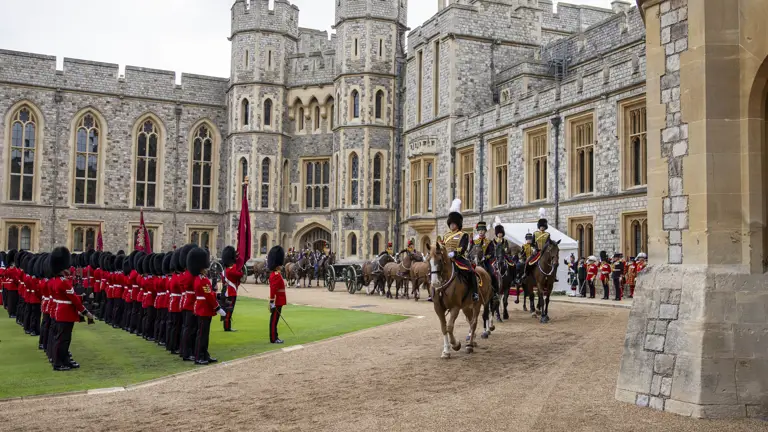 Mounted guards in ceremonial uniforms ride horses past a formation of soldiers in red coats and bearskin hats.