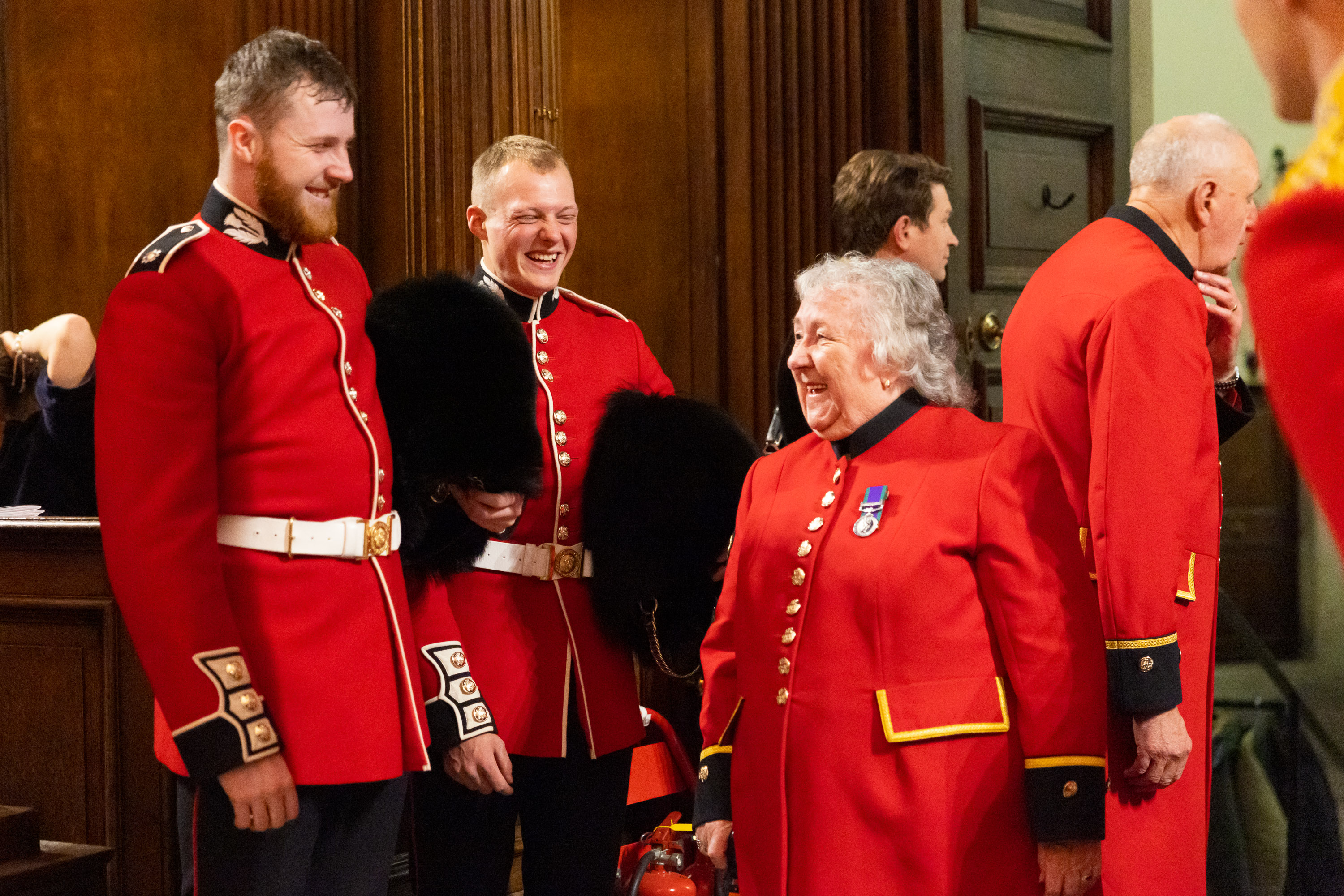 Group of people in traditional red Army uniforms standing indoors near wooden panelling and stone walls.