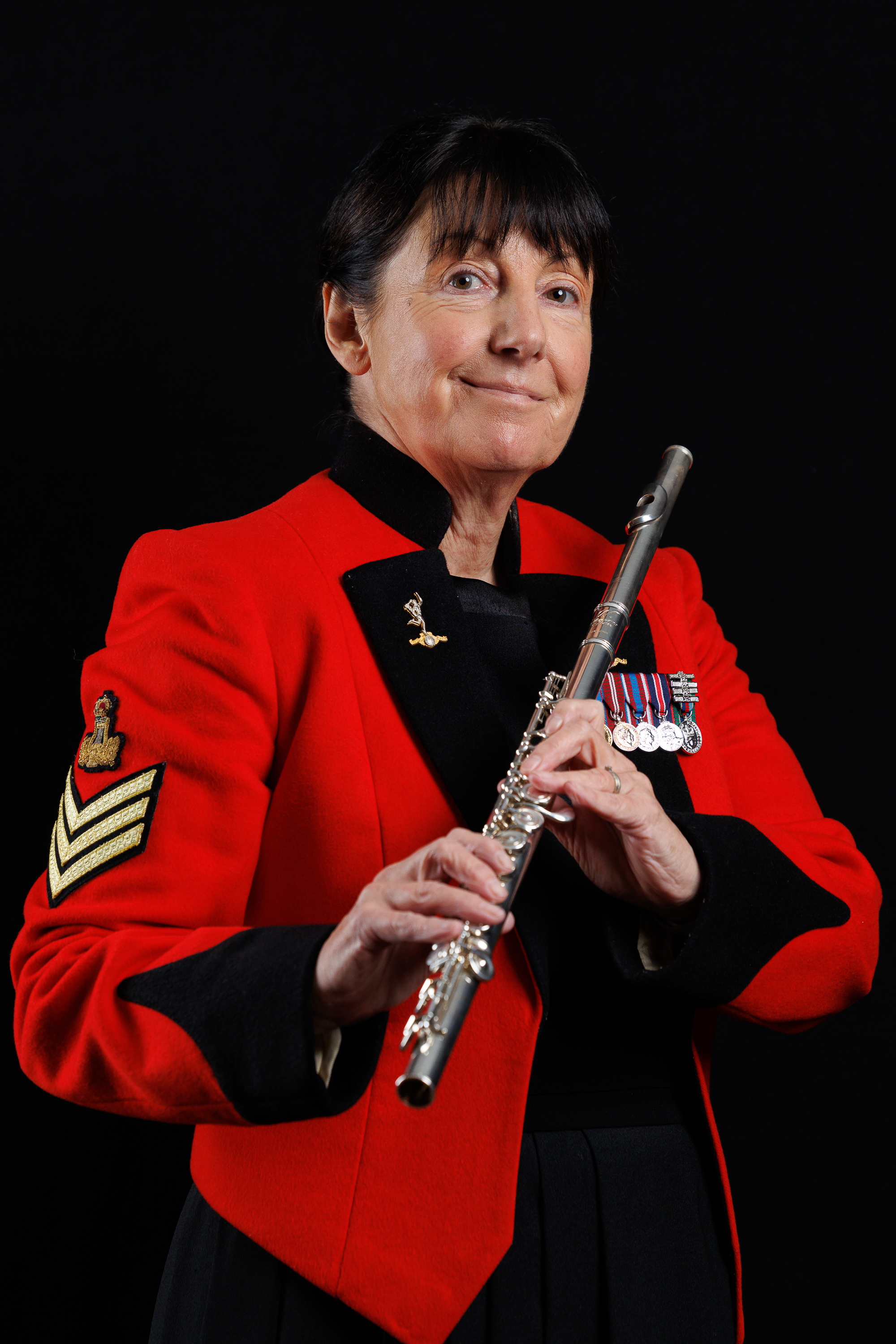  Musician in a red military-style jacket holding a silver flute against a black background.
