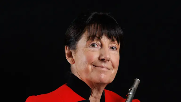 Musician in a red military-style jacket holding a silver flute against a black background.