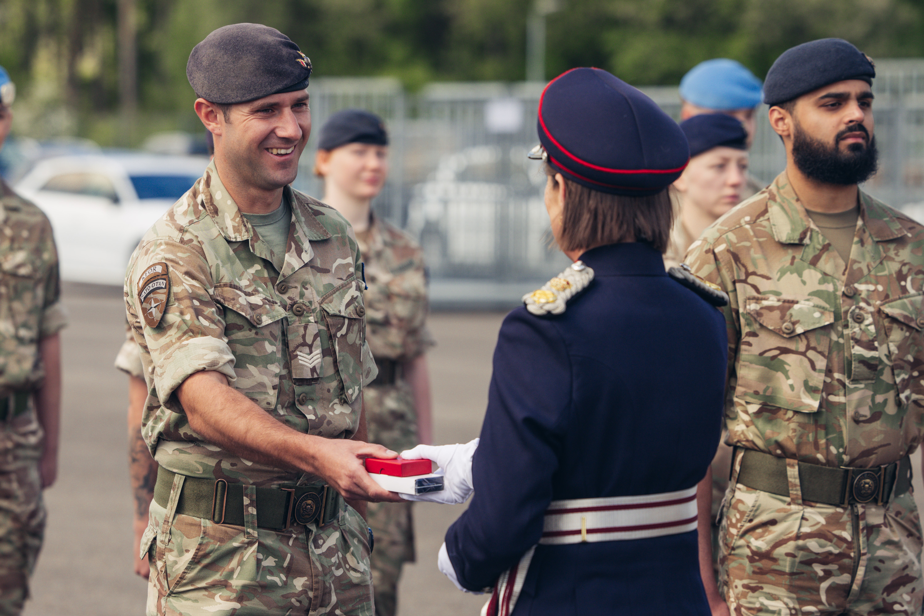 A soldier in uniform smiles as a woman in ceremonial attire hands him a medal.