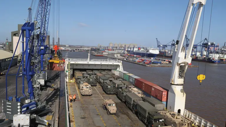 A bird's eye view of many green and brown Army vehicles on a ship.