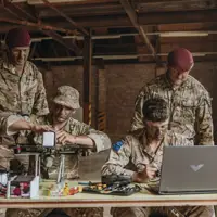 Four soldiers in camouflage uniforms work together on drone assembly inside of a warehouse with exposed brick walls.