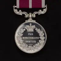 The medal is a silver metal engraves with a queen's crown and wreath. In the centre of the medal are the words