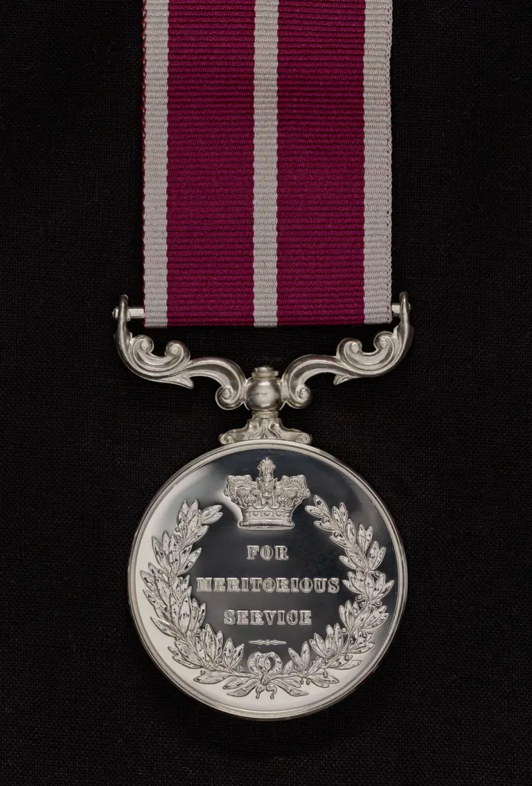 The medal is a silver metal engraves with a queen's crown and wreath. In the centre of the medal are the words