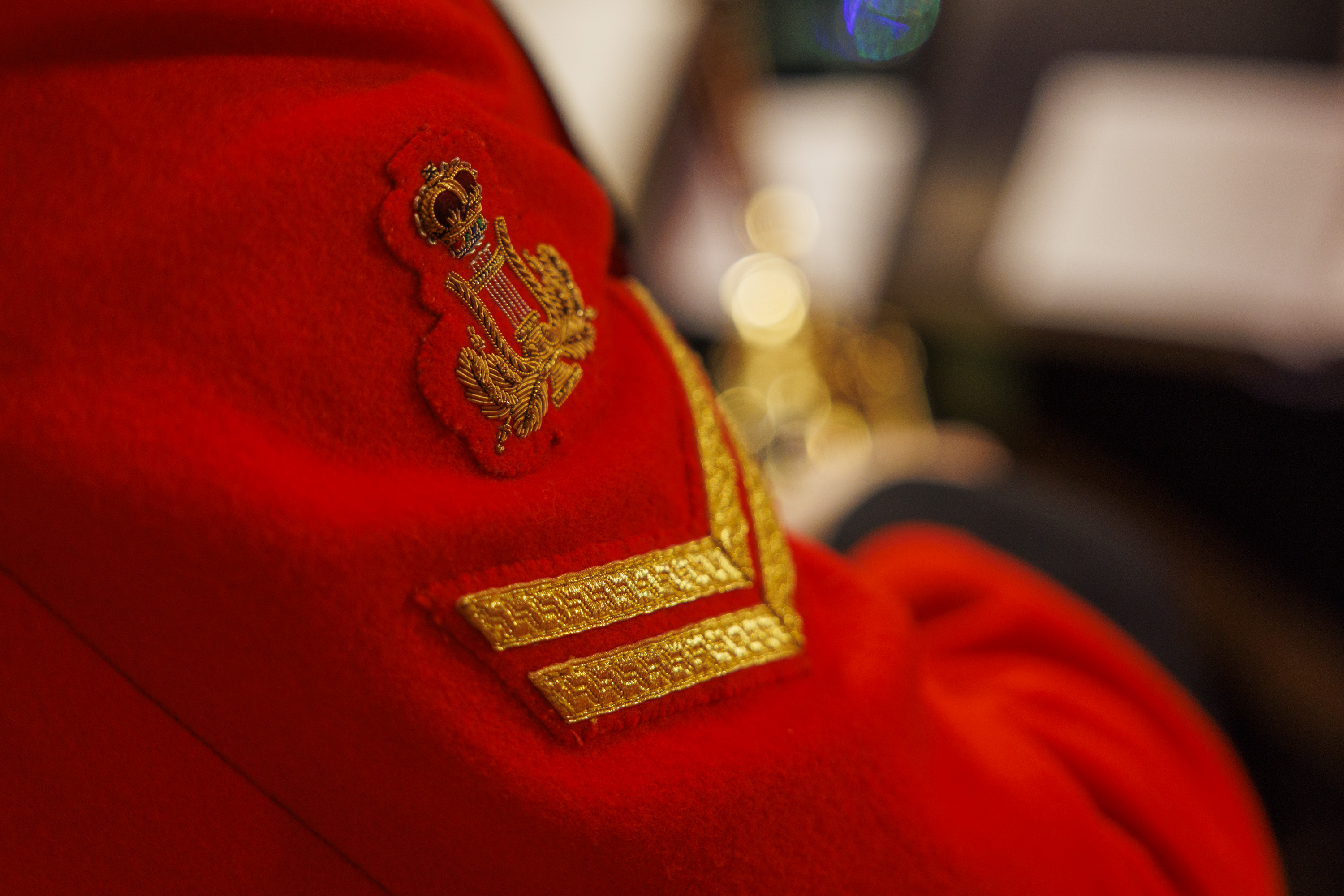 Close-up of a red military uniform sleeve with gold insignia and a crown emblem on a blurred background.