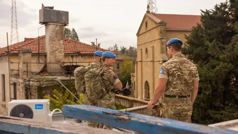 Three soldiers wearing uniform and blue berets are pictured on a rooftop overlooking a church.