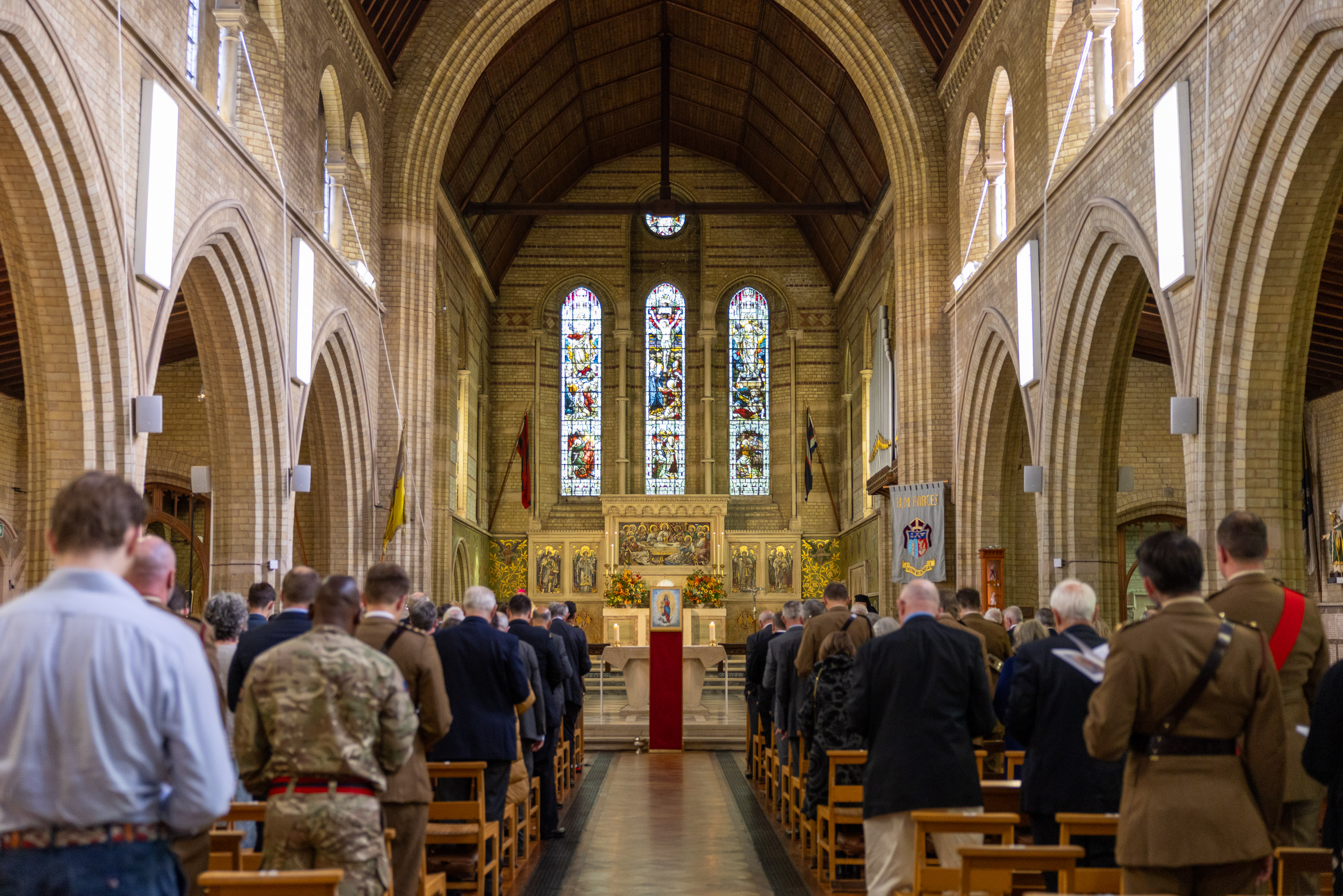 Interior of a large church with high arched ceilings, stained glass windows, and a congregation standing during a service.