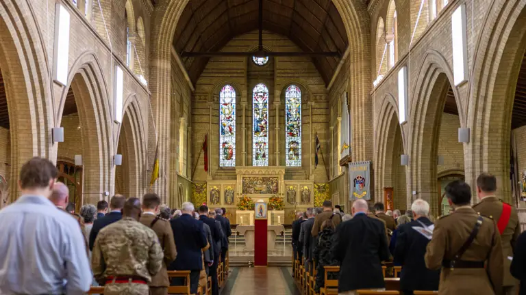 Interior of a large church with high arched ceilings, stained glass windows, and a congregation standing during a service.