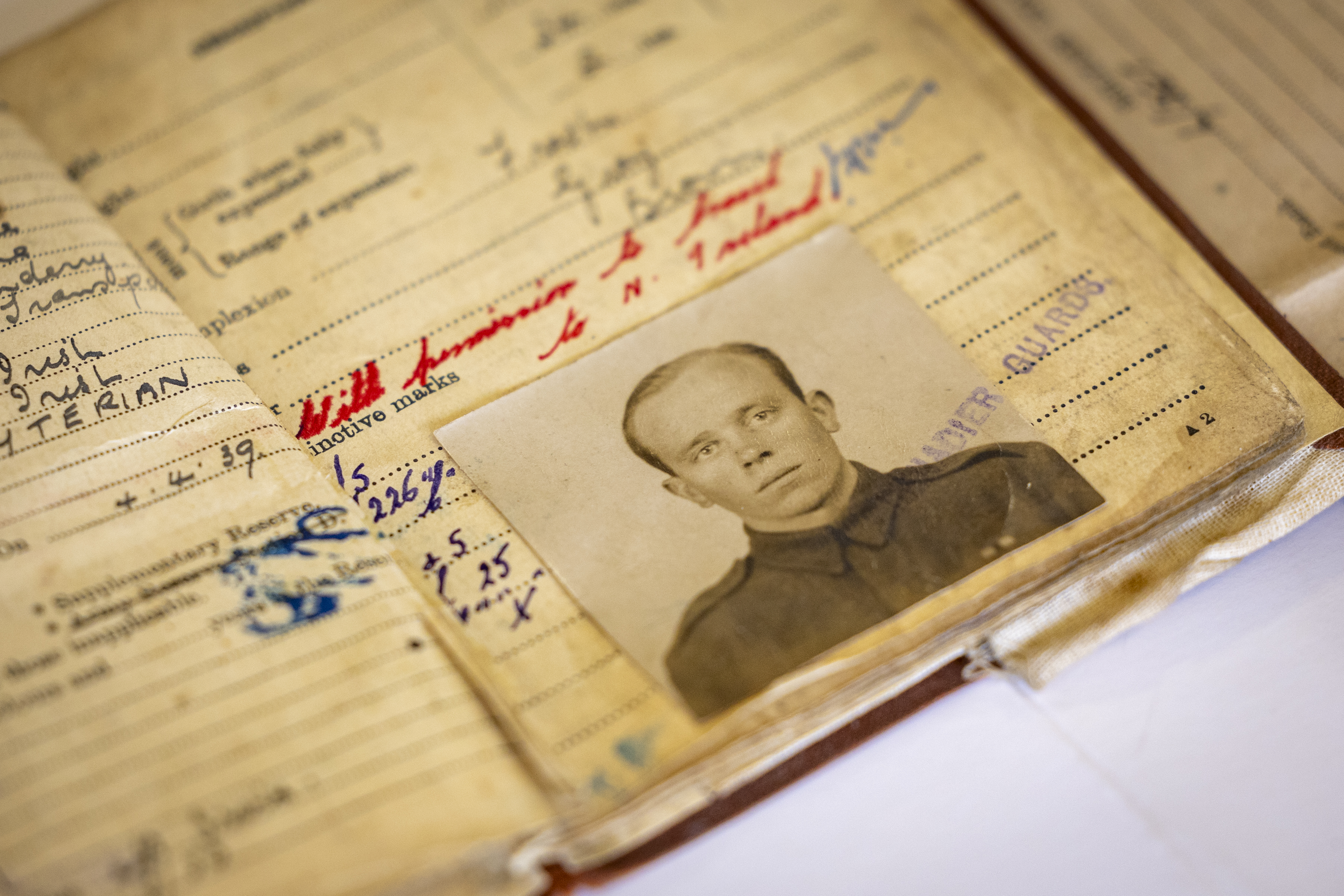 Old military record book opened to a page with handwritten notes and a black-and-white portrait photo of a soldier in uniform.