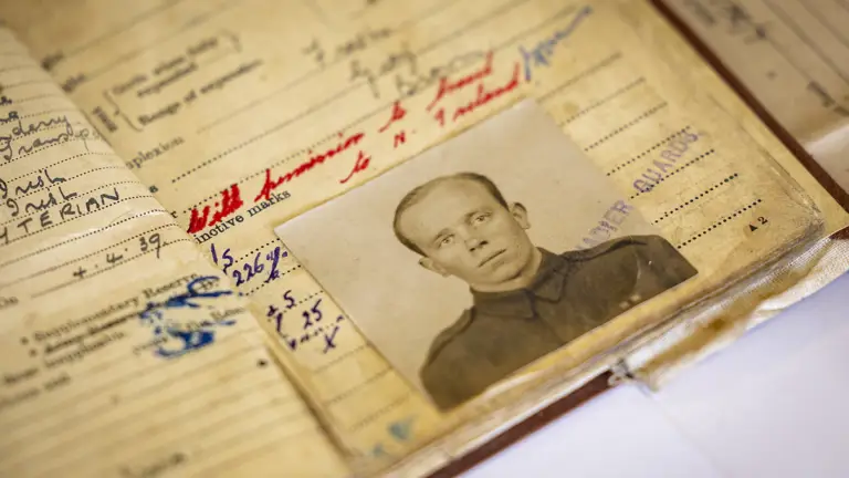 Old military record book opened to a page with handwritten notes and a black-and-white portrait photo of a soldier in uniform.