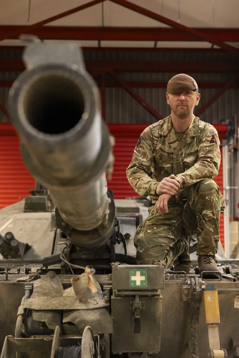 A man in uniform sits on top of a tank.