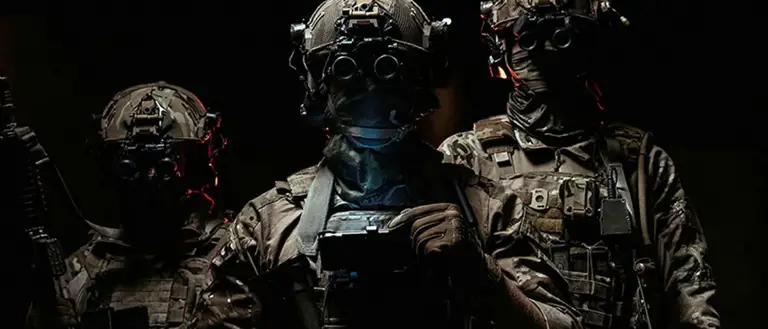 Three soldiers in combat gear wearing night vision goggles in a dark environment.