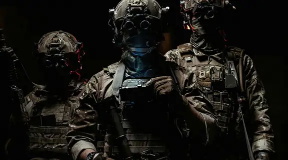 Three soldiers in combat gear wearing night vision goggles in a dark environment.