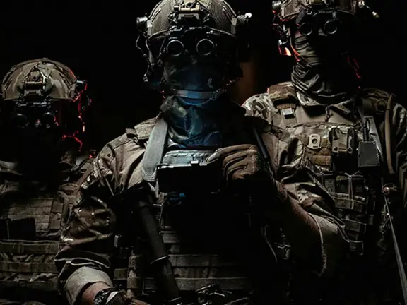 Three soldiers in combat gear wearing night vision goggles in a dark environment.
