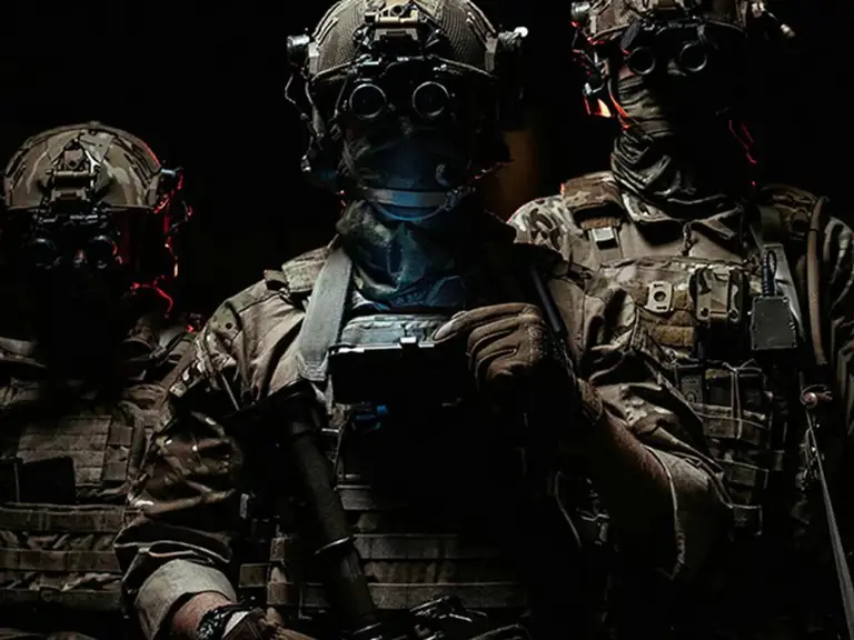 Three soldiers in combat gear wearing night vision goggles in a dark environment.