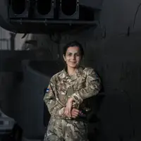 A person in military uniform stands in front of a helicopter with