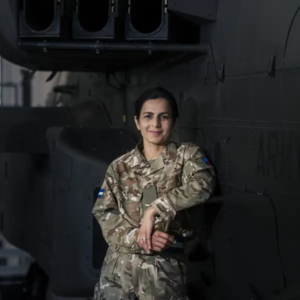 A person in military uniform stands in front of a helicopter with