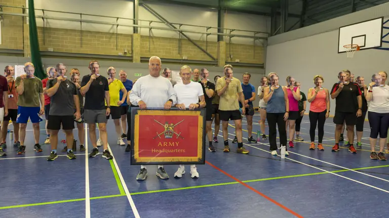 People wearing fitness clothes stand behind two people in the front of the image. The two of the front are holding a frame with a red flag in it.