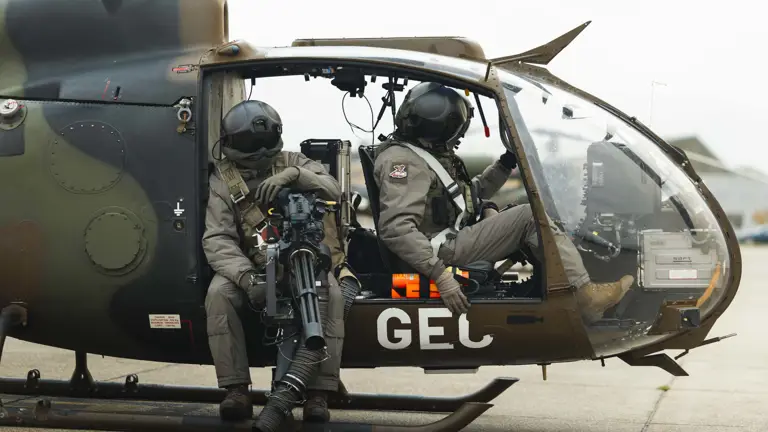 Two soldiers in full tactical gear seated inside a military helicopter.