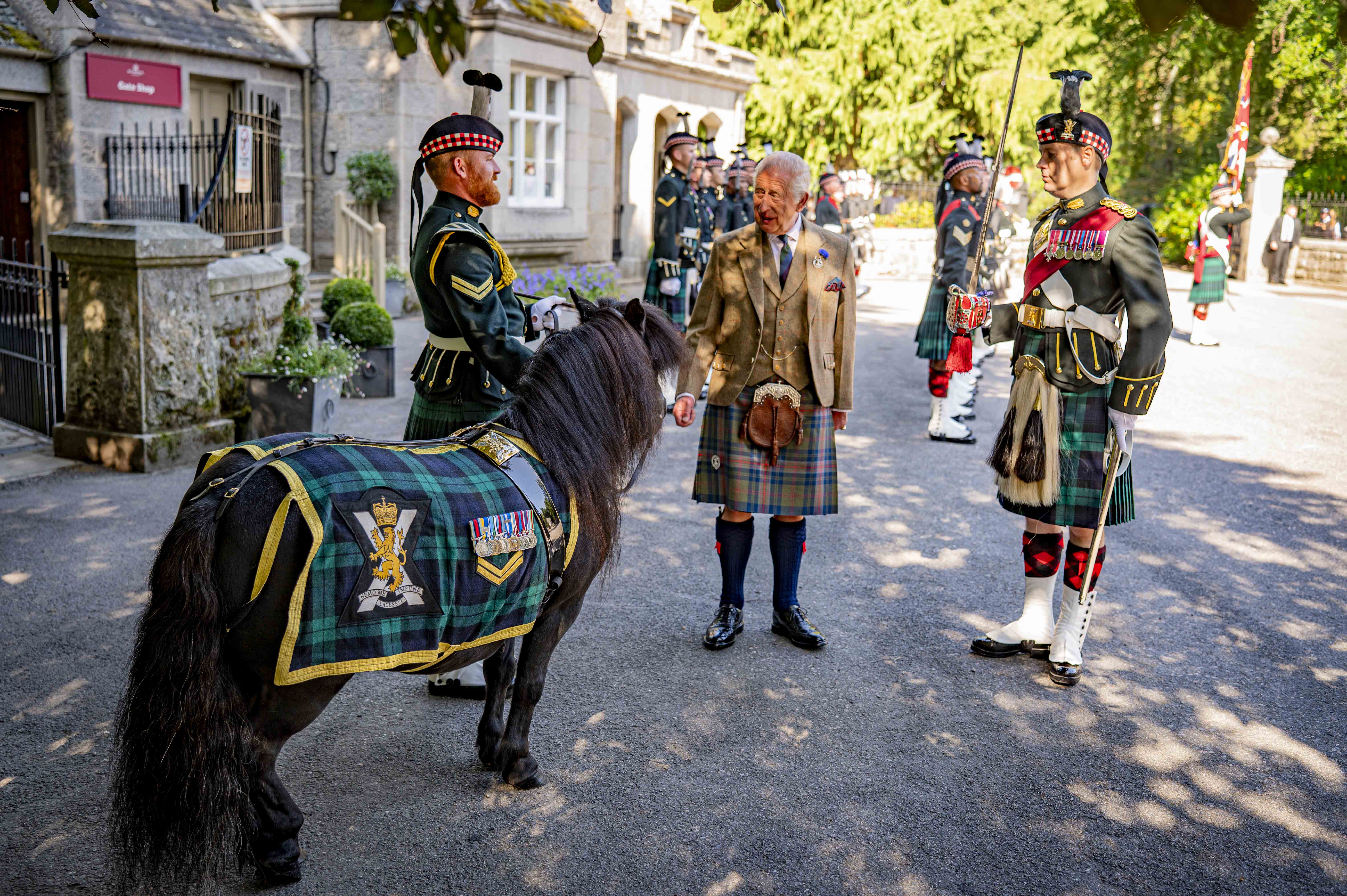 Scottish soldiers in traditional military dress stand with His Majesty The King in a kilt beside a pony draped in tartan.