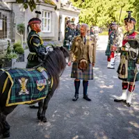 Scottish soldiers in traditional military dress stand with His Majesty The King in a kilt beside a pony draped in tartan.