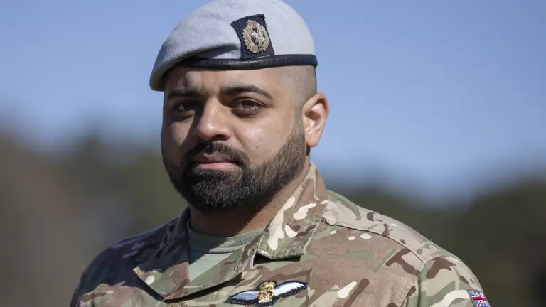 Soldiers in his camouflage unifrom with his arms behind his back and light blue berets on their heads stood outside.