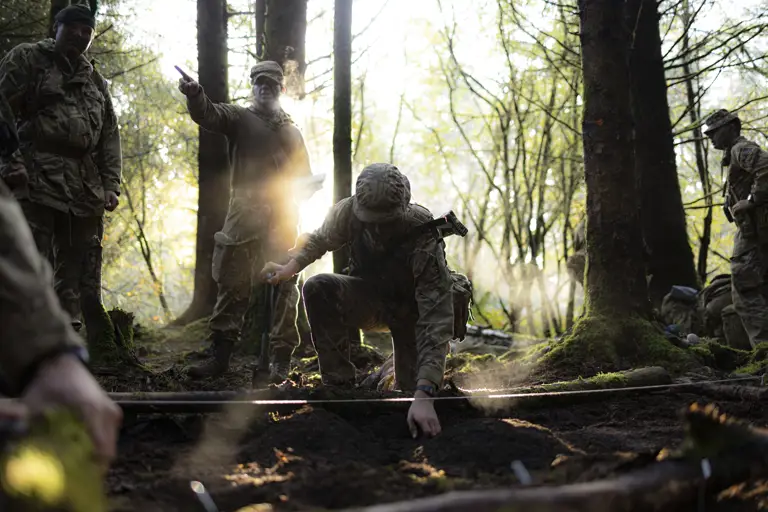 Several soldiers in uniform are pictured within a woodland on exercise. 