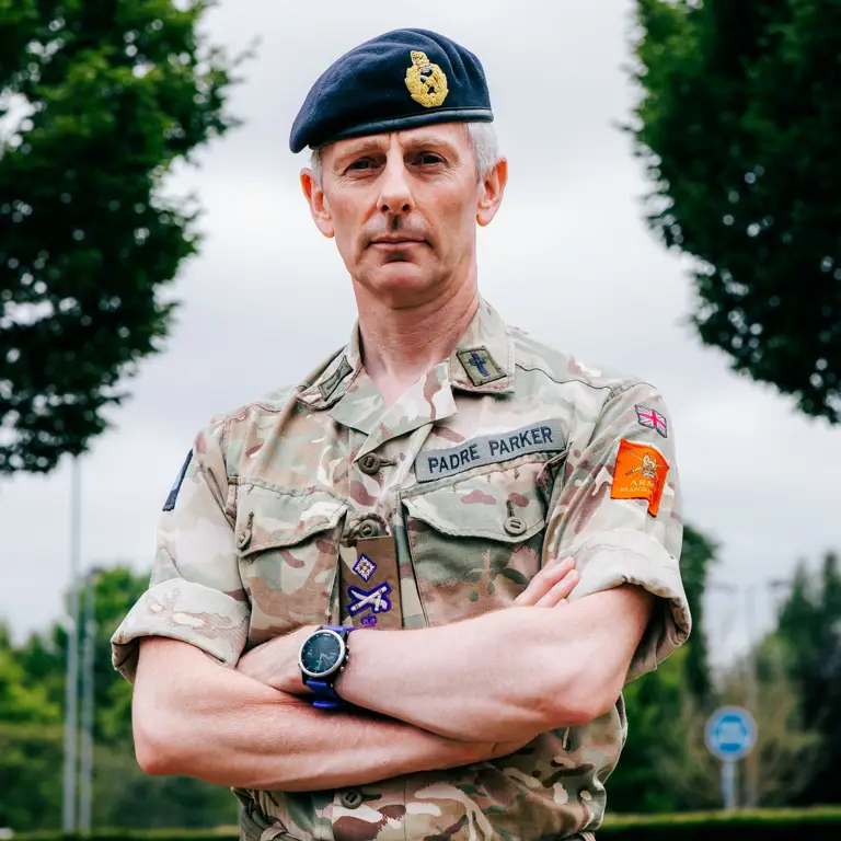 Reverend Canon Michael Parker, stood with his arms folded posing for a portrait while wearing his uniform and beret.