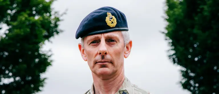 Reverend Canon Michael Parker, stood with his arms folded posing for a portrait while wearing his uniform and beret.