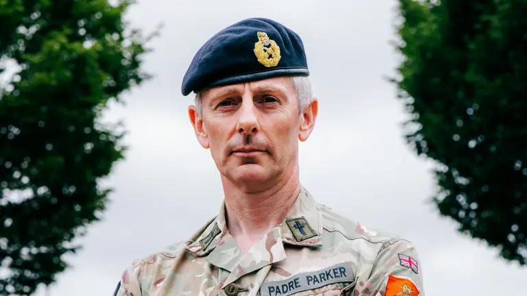 Reverend Canon Michael Parker, stood with his arms folded posing for a portrait while wearing his uniform and beret.