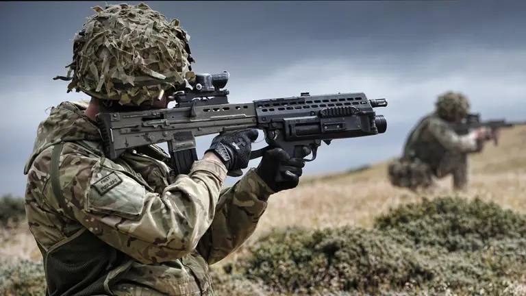 A soldier takes aim with their rifle. Attached underneath the barrel is a grenade launcher.