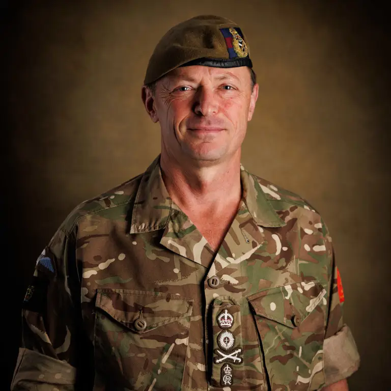 Person wearing a camouflage military uniform with rolled-up sleeves and a tan beret featuring an insignia.