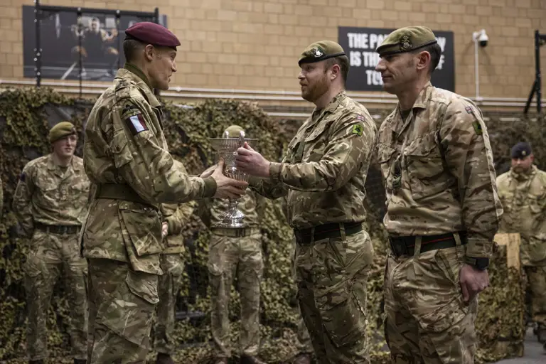 Two men in uniform are presented a trophy by a man in uniform.