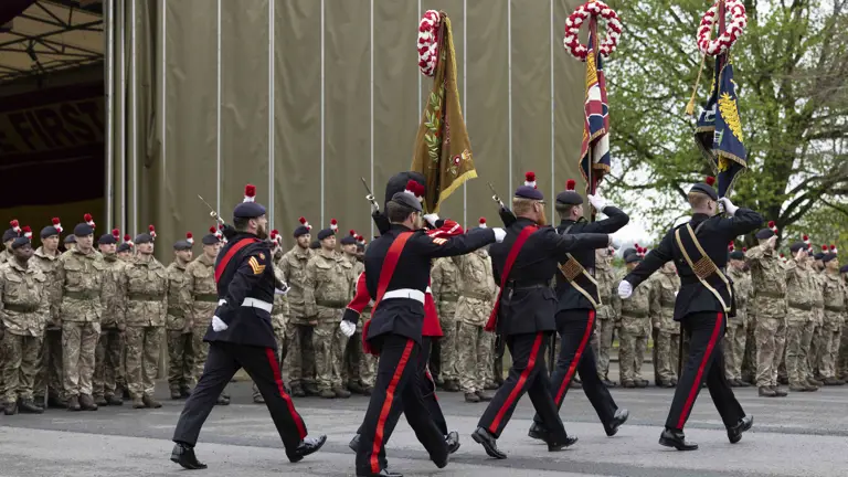 Soldiers in black ceremonial uniforms march past soldiers in green camouflage uniforms.