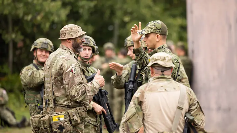 soldiers from both the British Army and the Croatian Armed Forces stand talking outside a building on exercise wearing their different camouflage uniforms