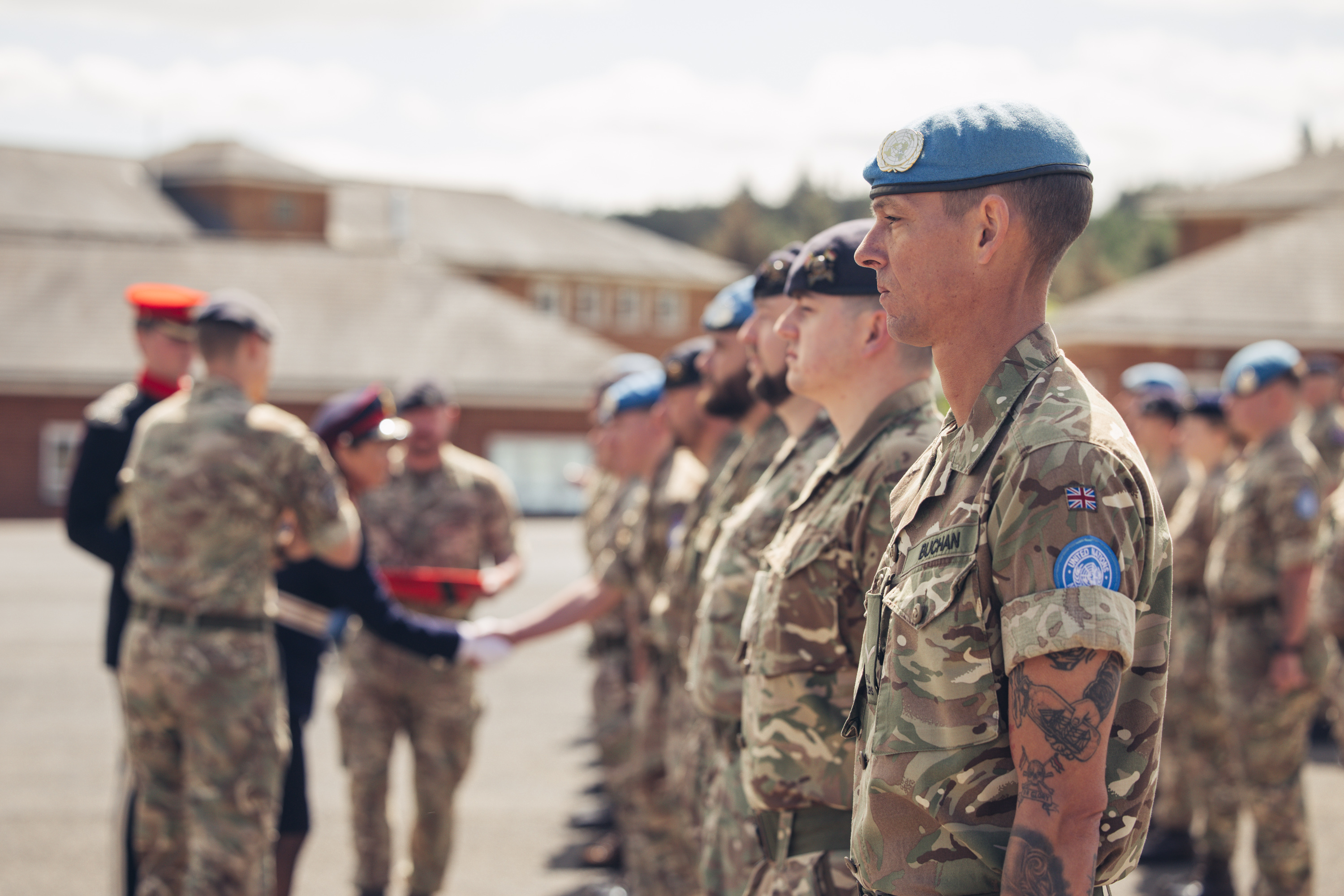 A line of soldiers in uniform awaiting medals, some are wearing light blue berets. 
