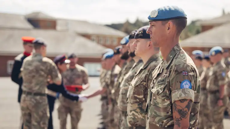 A line of soldiers in uniform awaiting medals, some are wearing light blue berets.