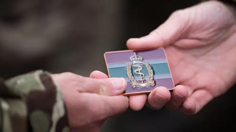 A token with the new Royal Army Medical Services logo is handed to a soldier in uniform.