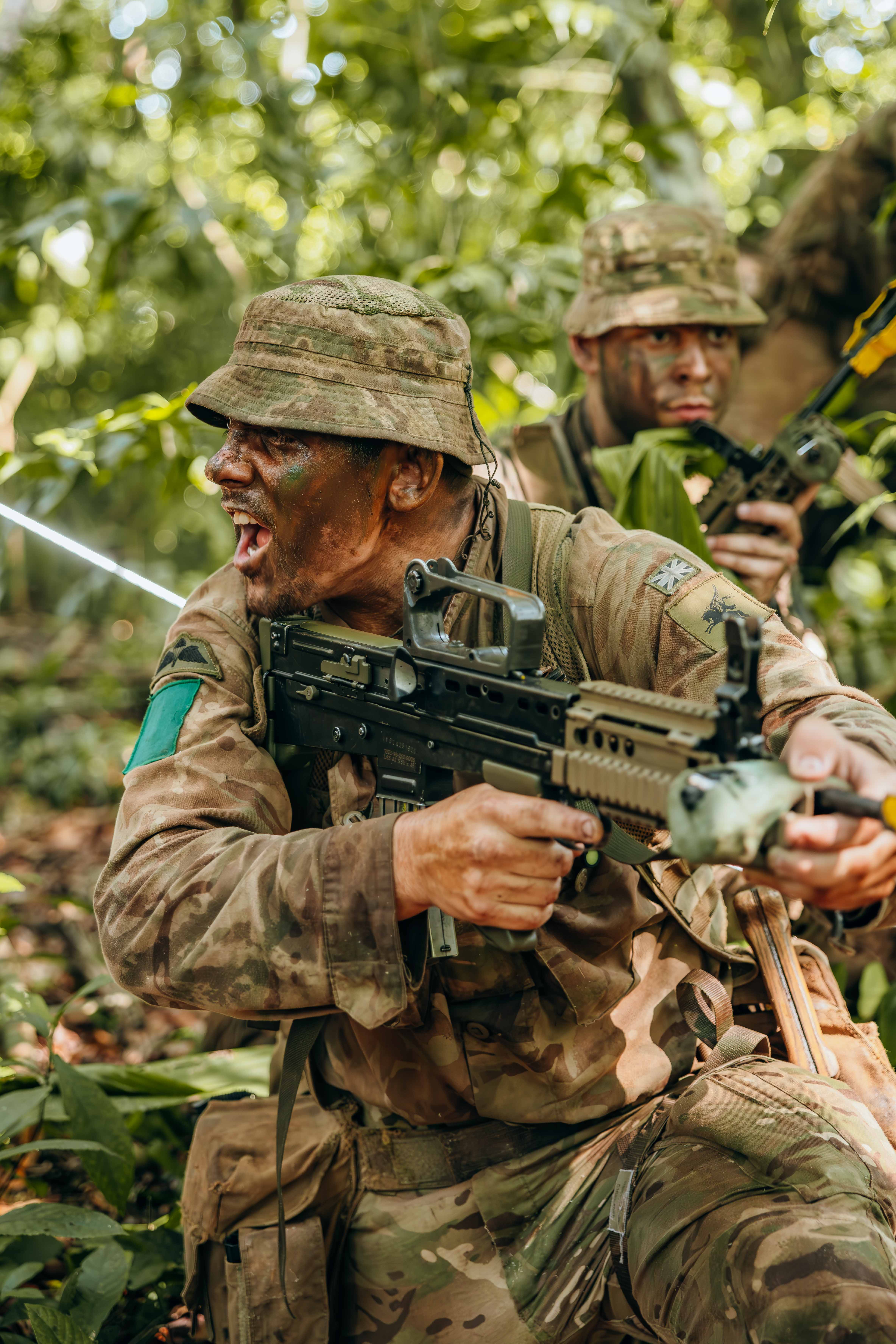Soldier in camouflage gear aiming a rifle while crouching in dense jungle foliage during a tactical operation.