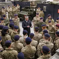 A group of uniformed soldiers wearing berets gathered around a man in civilian clothes speaking to them.